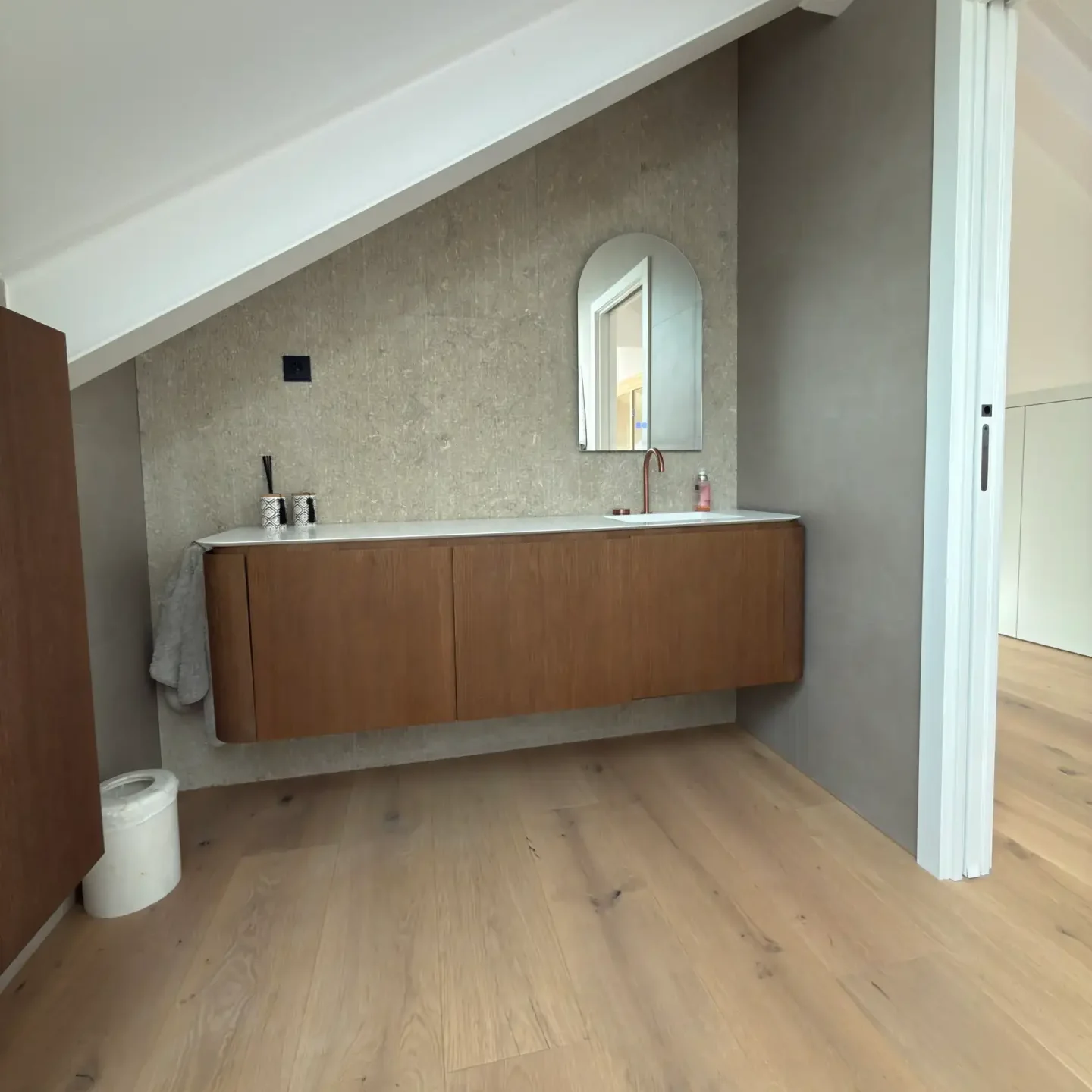 Baño moderno con revestimiento microcemento gris y mueble de lavabo suspendido en madera.
