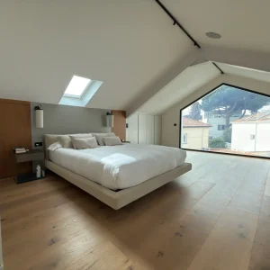 Dormitorio principal abuhardillado tipo suite con ventana Velux y tarima flotante de madera.