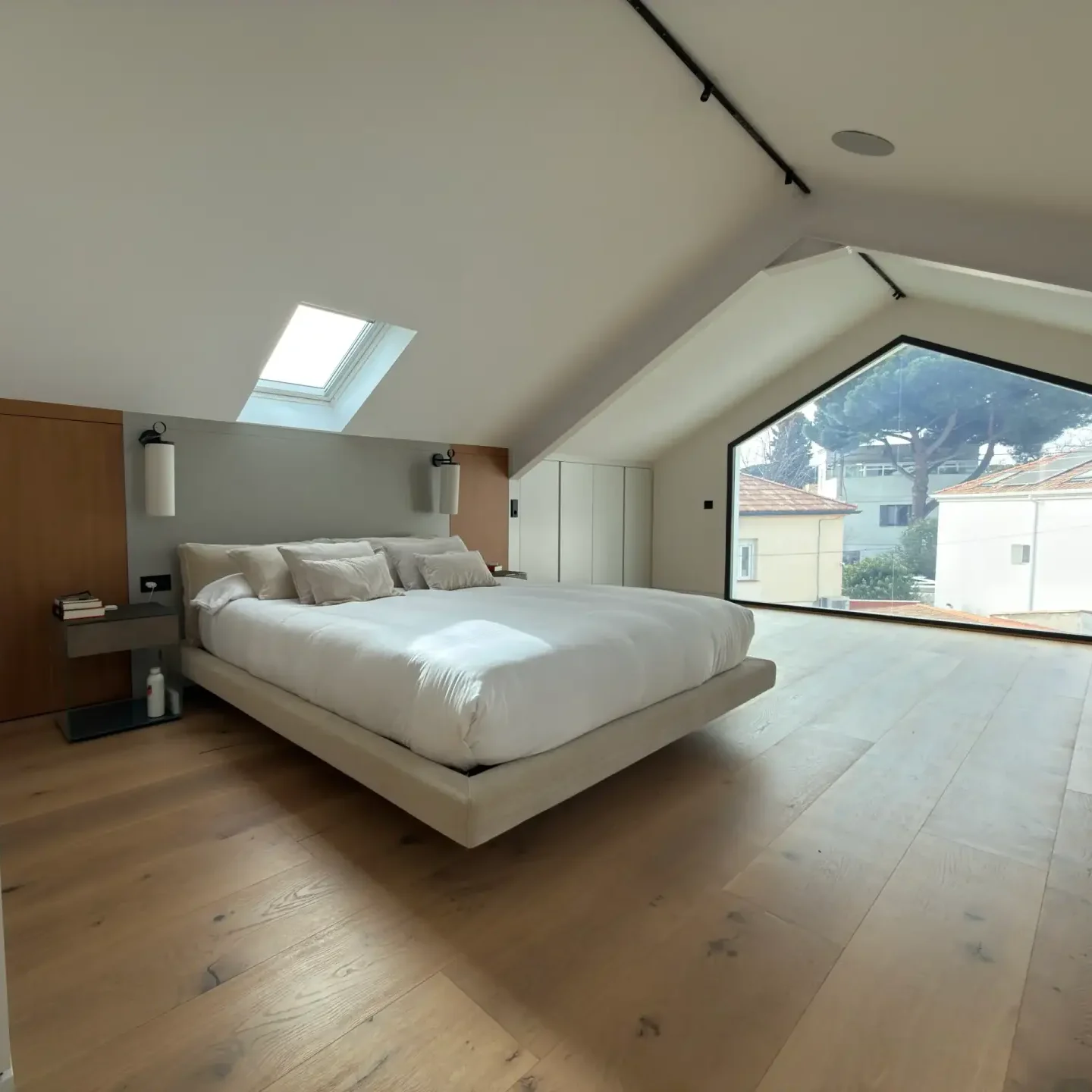Dormitorio principal abuhardillado tipo suite con ventana Velux y tarima flotante de madera.