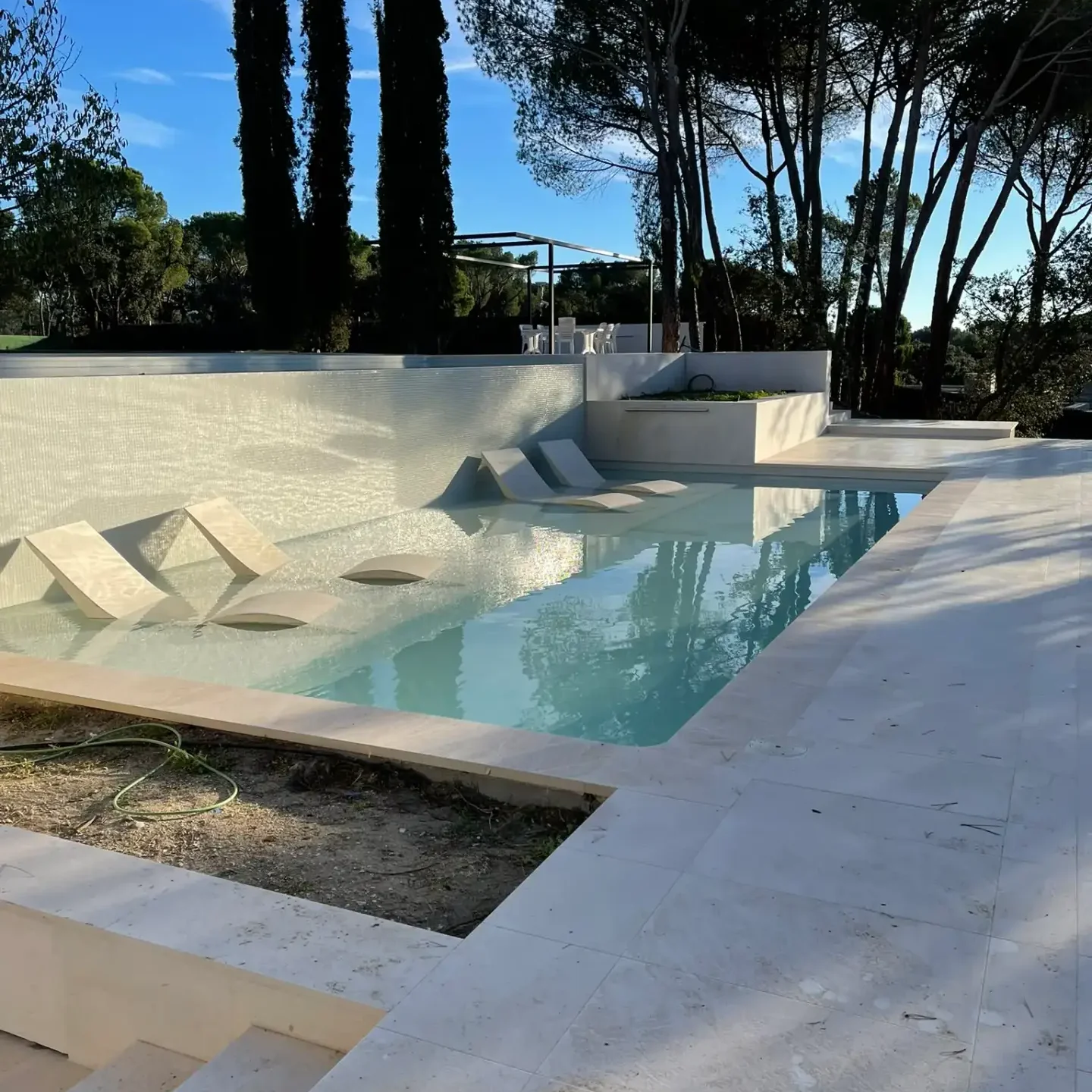 Área de solárium con tumbonas integradas en una playa de piscina moderna rodeada de vegetación.