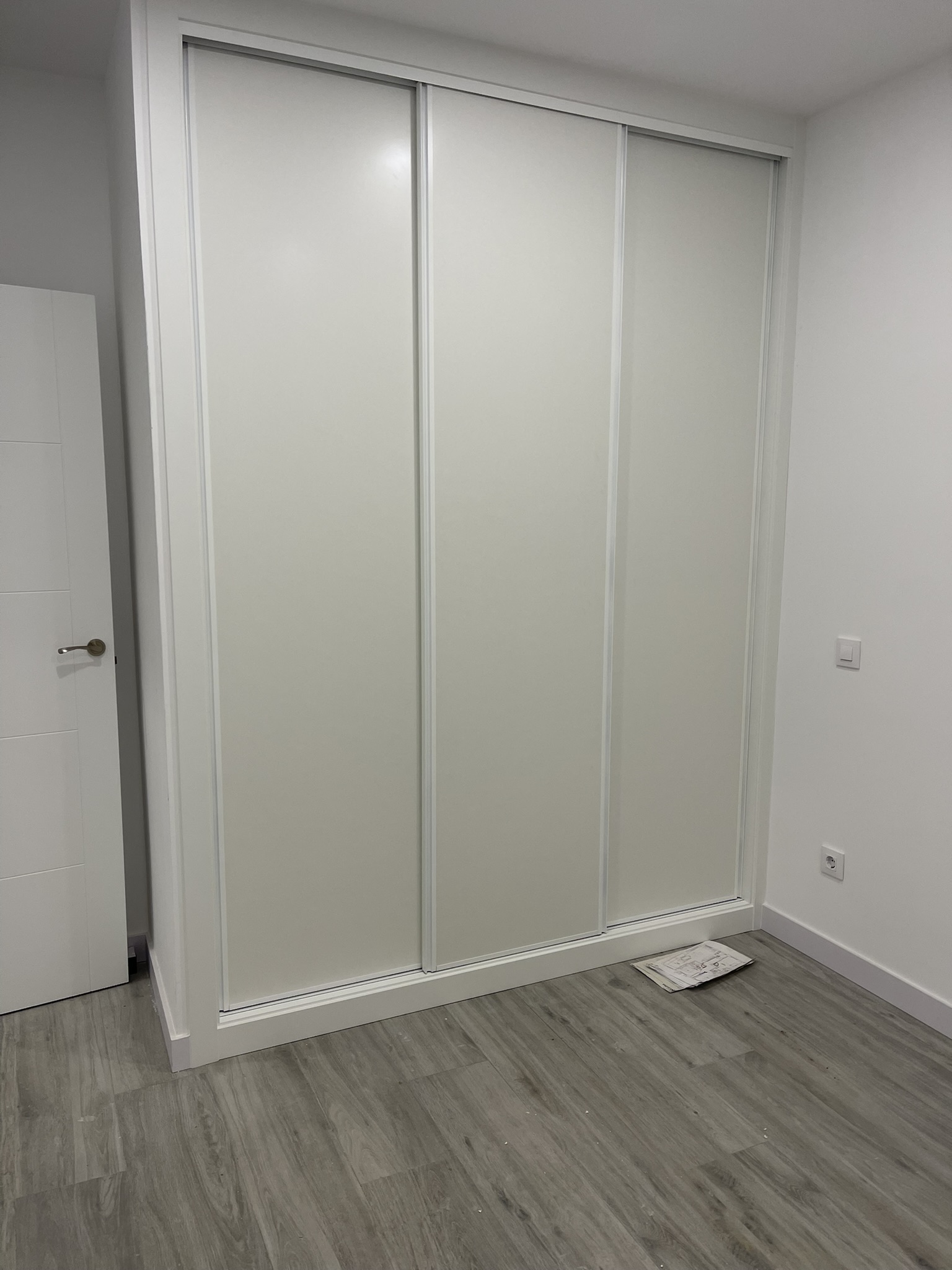 Armario empotrado de puertas correderas blancas y tarima flotante en piso reformado
