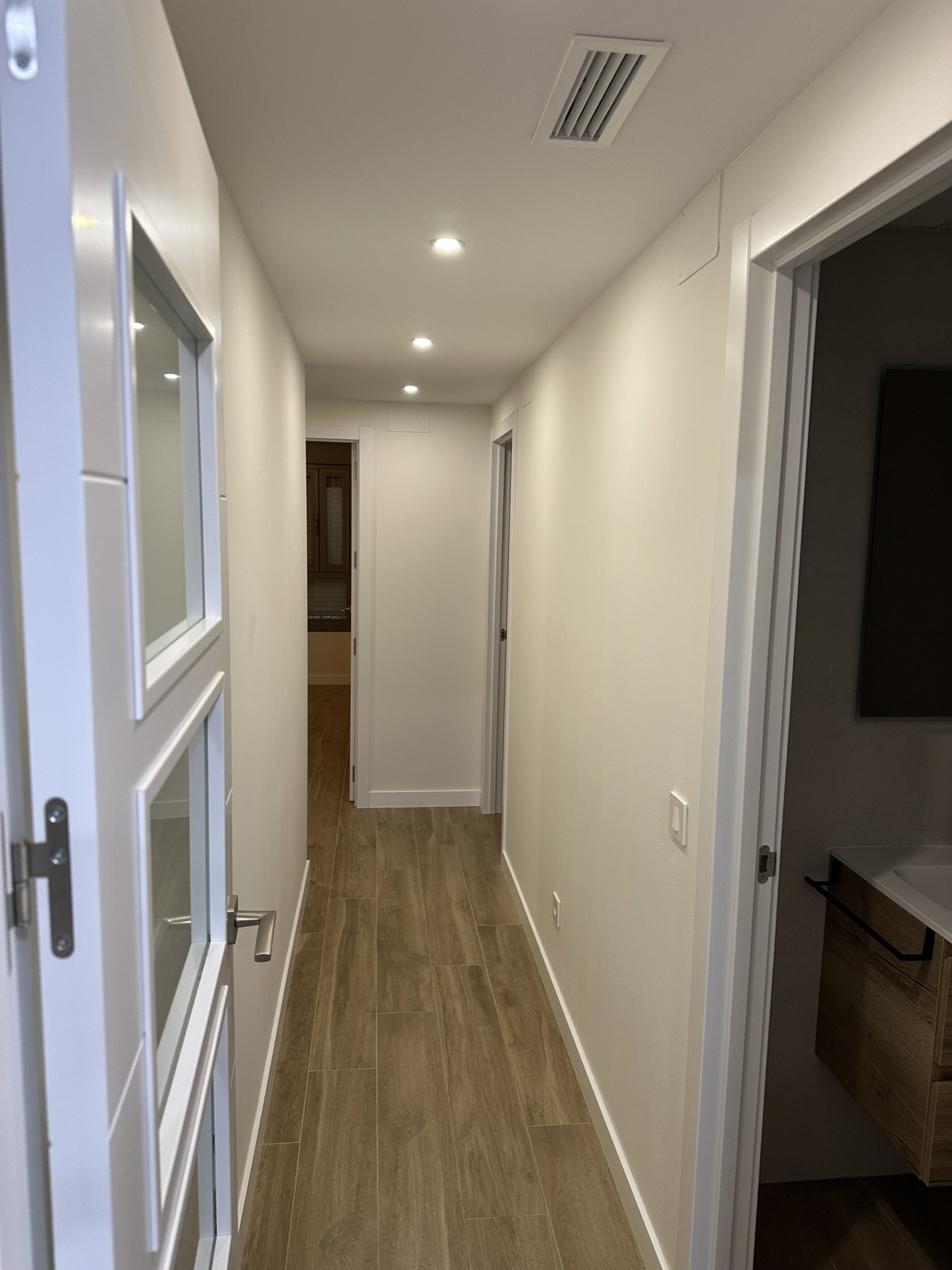 Pasillo de piso reformado con carpintería blanca interior y acceso a baño al fondo