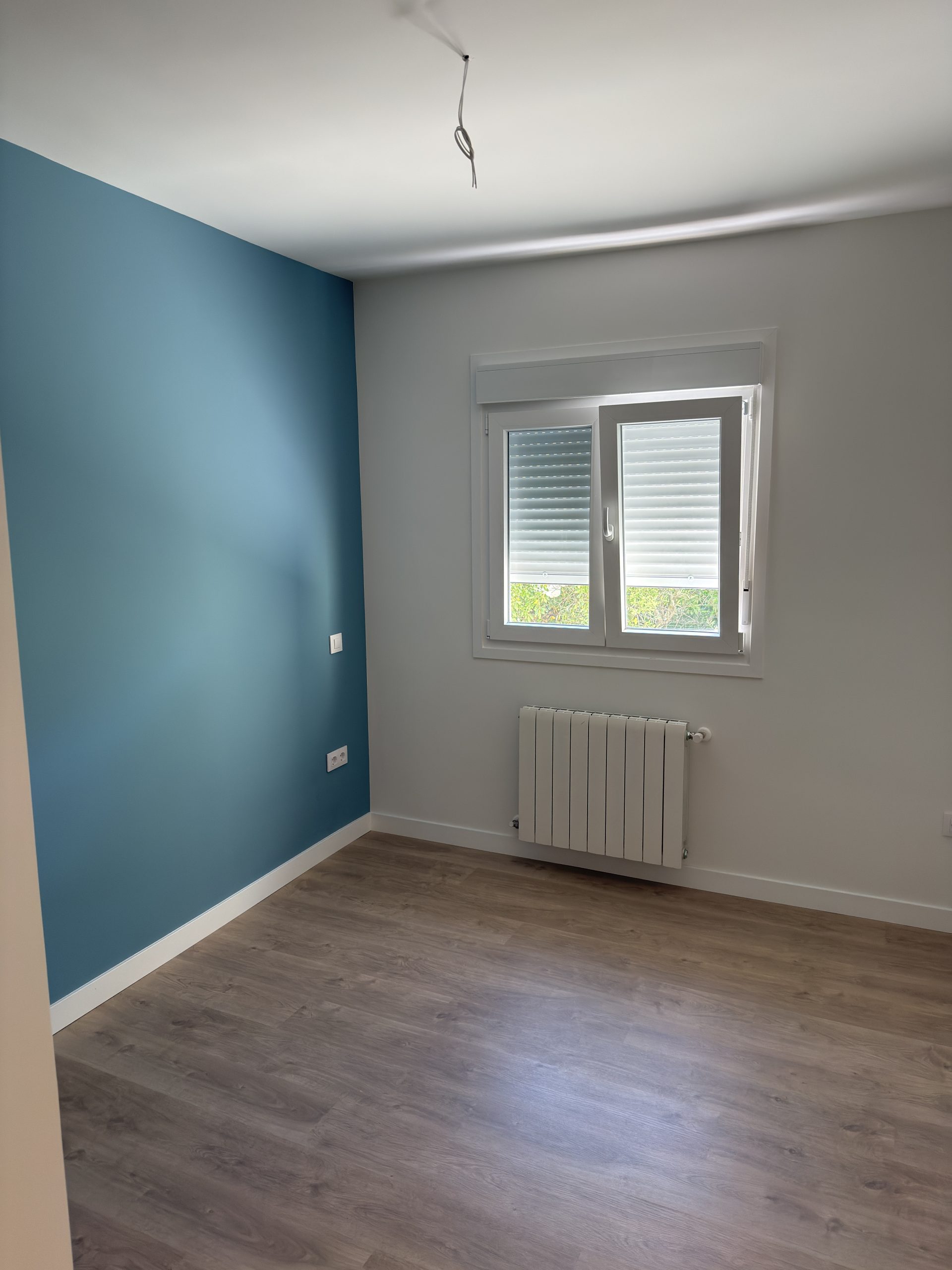 Habitación reformada con pared azul de contraste, tarima y radiador nuevo en Madrid