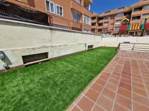 Zona comunitaria con césped artificial y solado cerámico exterior en Madrid