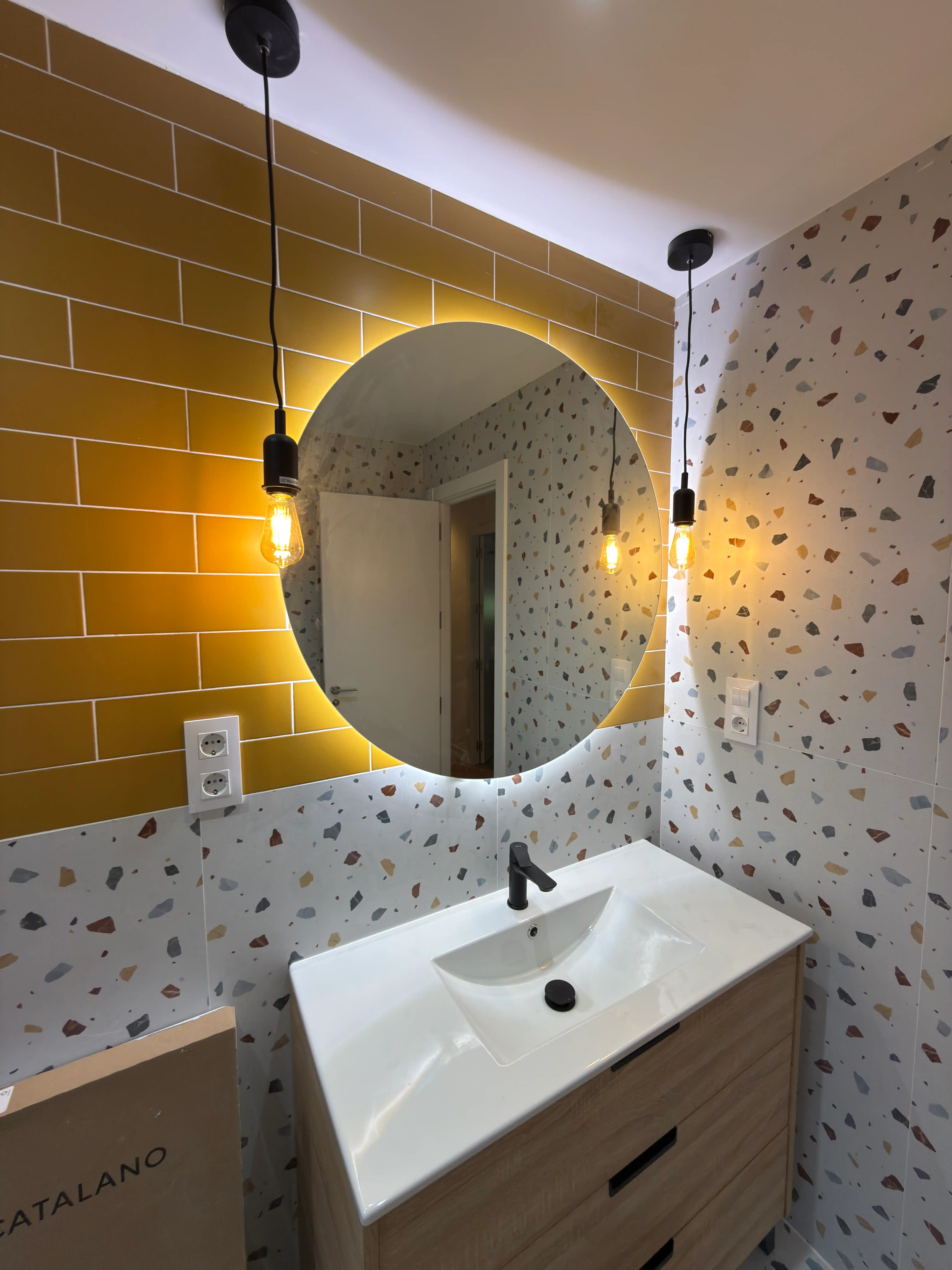 Lavabo de diseño con espejo redondo, luces colgantes e iluminación cálida en baño contemporáneo.