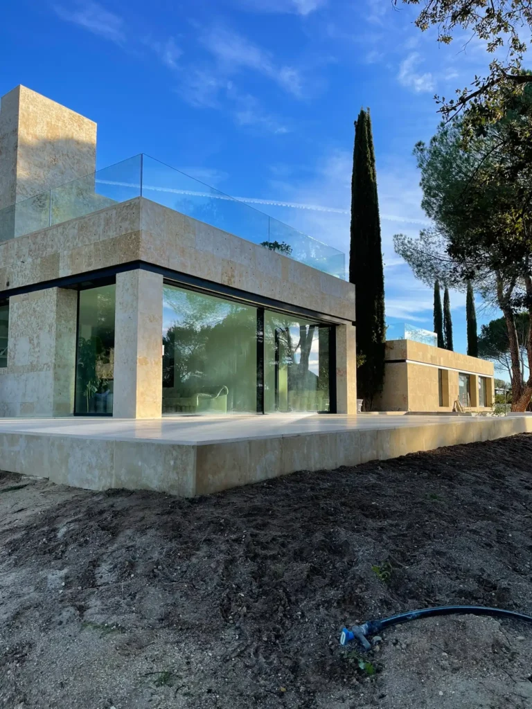 Detalle de fachada moderna con cerramientos de cristal de suelo a techo y estructura envolvente revestida en piedra natural.