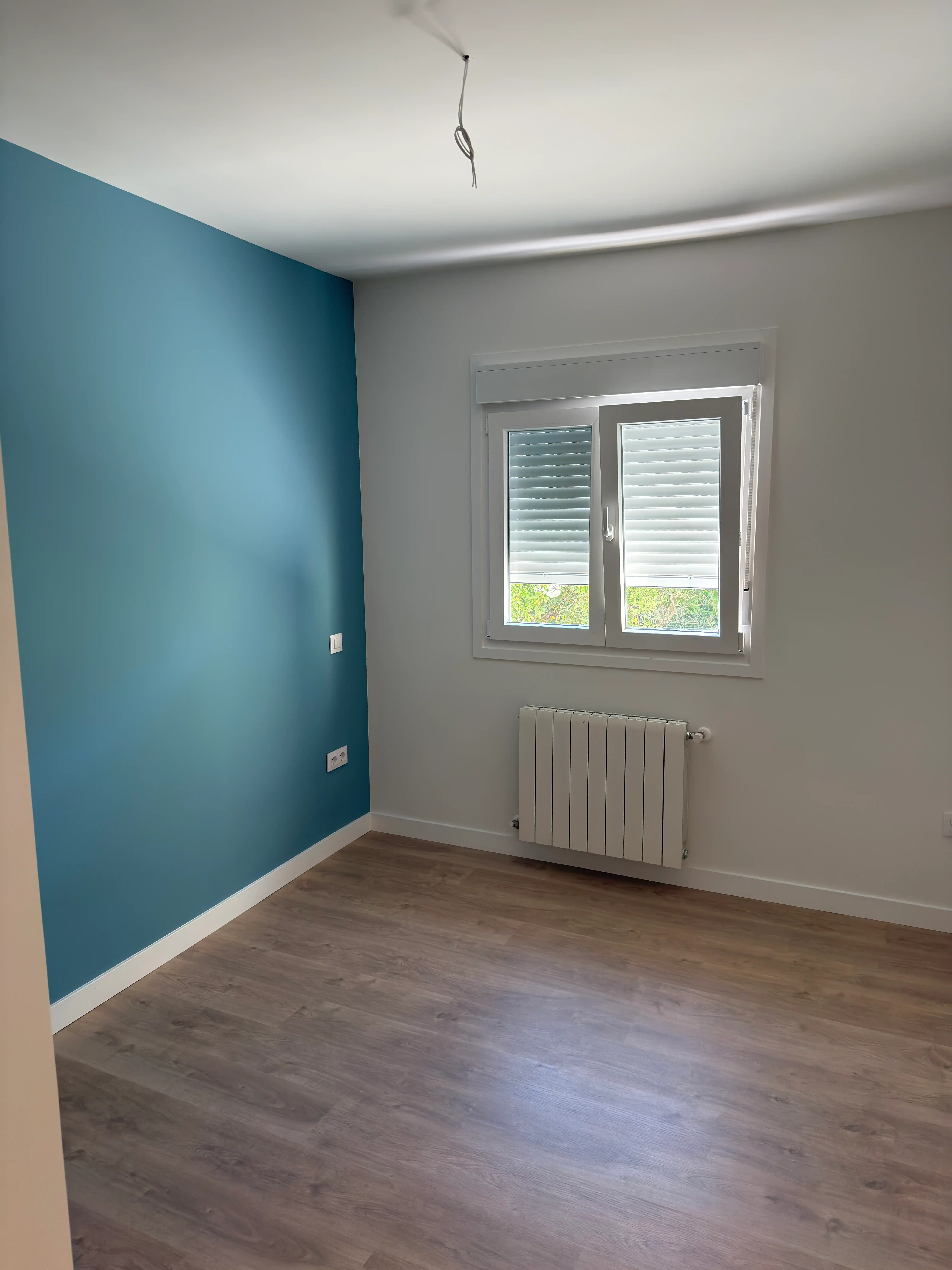 Dormitorio interior renovado con pintura azul y nueva ventana de PVC aislante.