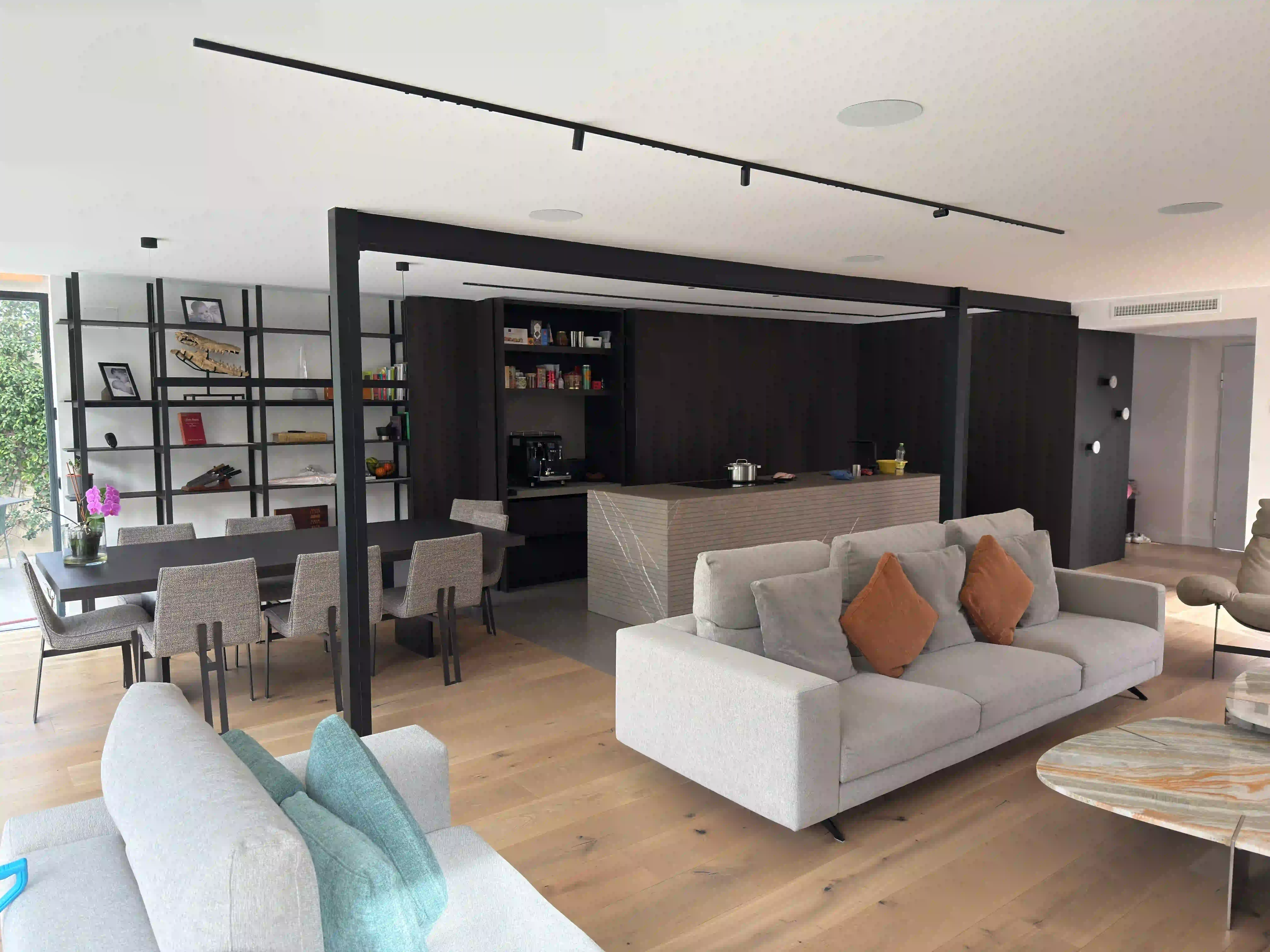 Diseño de interiores de concepto abierto con cocina integrada y salón, destacando elementos estructurales vistos en negro y suelo radiante de madera.