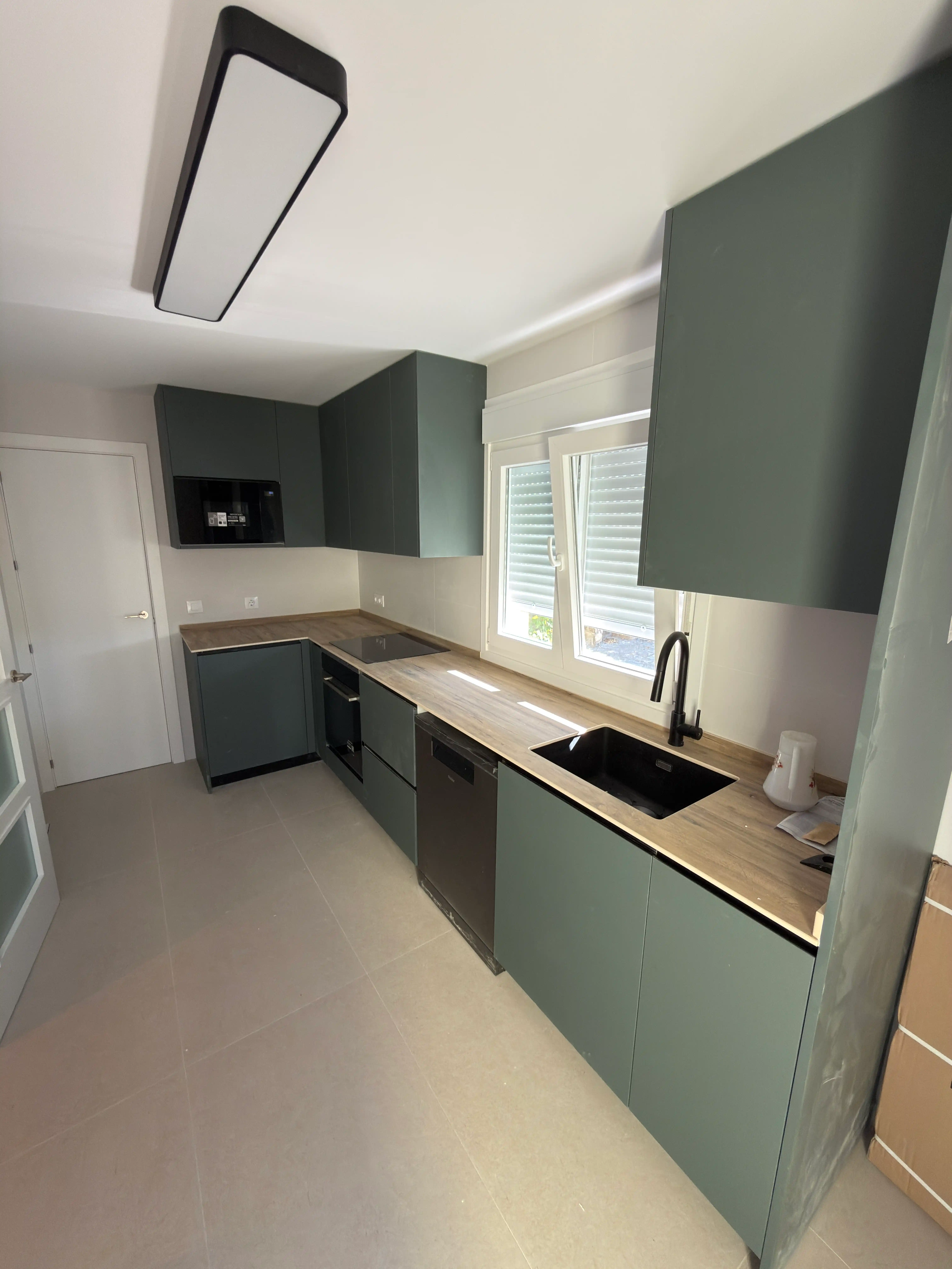 Perspectiva de los muebles de cocina a medida en tonos verdes y grises con encimera de madera.