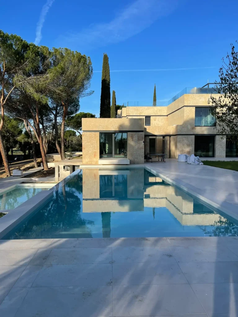 Gran piscina exterior de diseño moderno reflejando la fachada de piedra de Salamanca de una mansión de lujo rehabilitada.