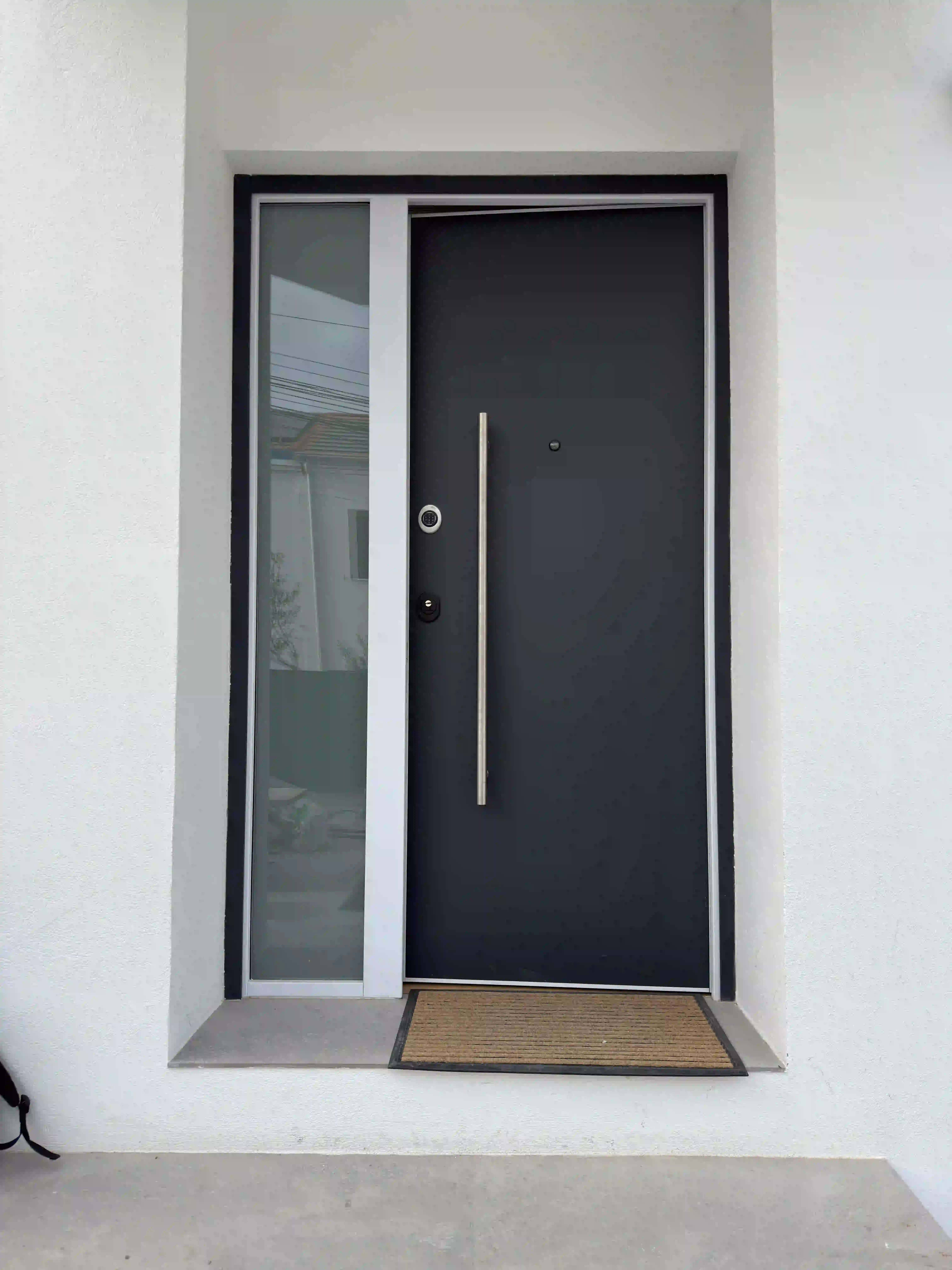 Puerta de entrada principal moderna en tonos oscuros con tirador de acero, instalada en reforma integral premium.