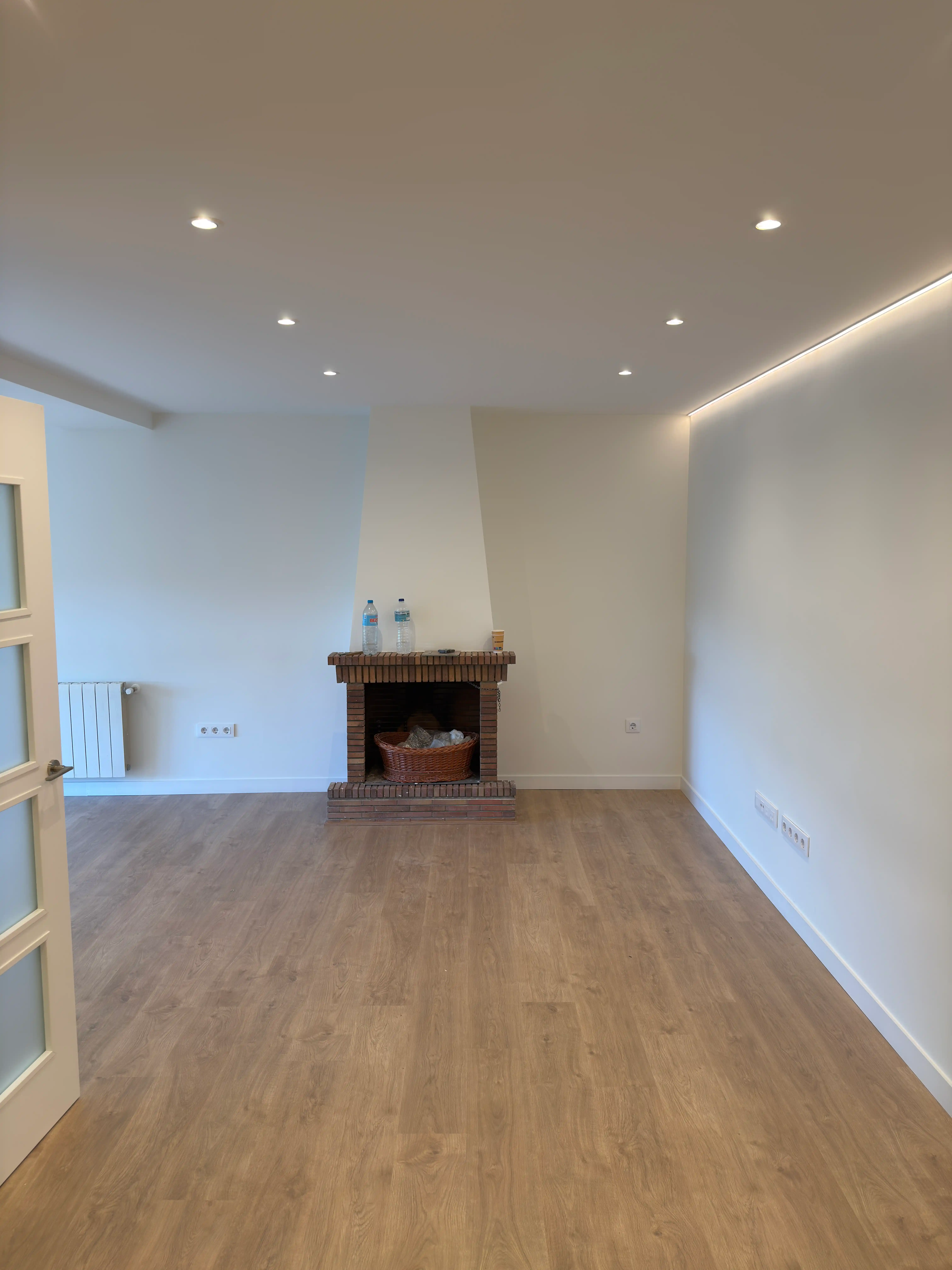 Salón diáfano con chimenea, suelo laminado y diseño de iluminación indirecta LED en el techo.