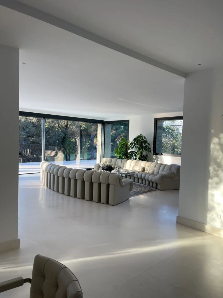 Espectacular salón de diseño minimalista con sofá modular curvo, pavimento continuo y cerramientos de gran formato que integran el espacio interior con los jardines de la finca.