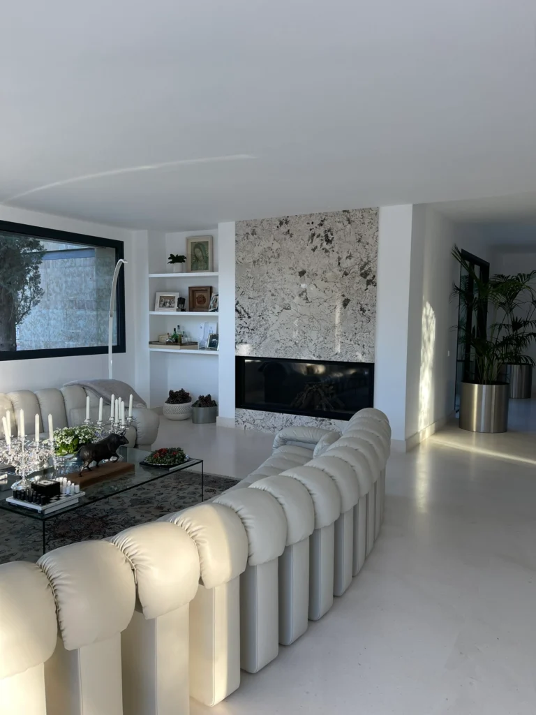 Salón de diseño contemporáneo con sofá curvo, imponente pared de mármol y chimenea integrada en vivienda de alto standing.