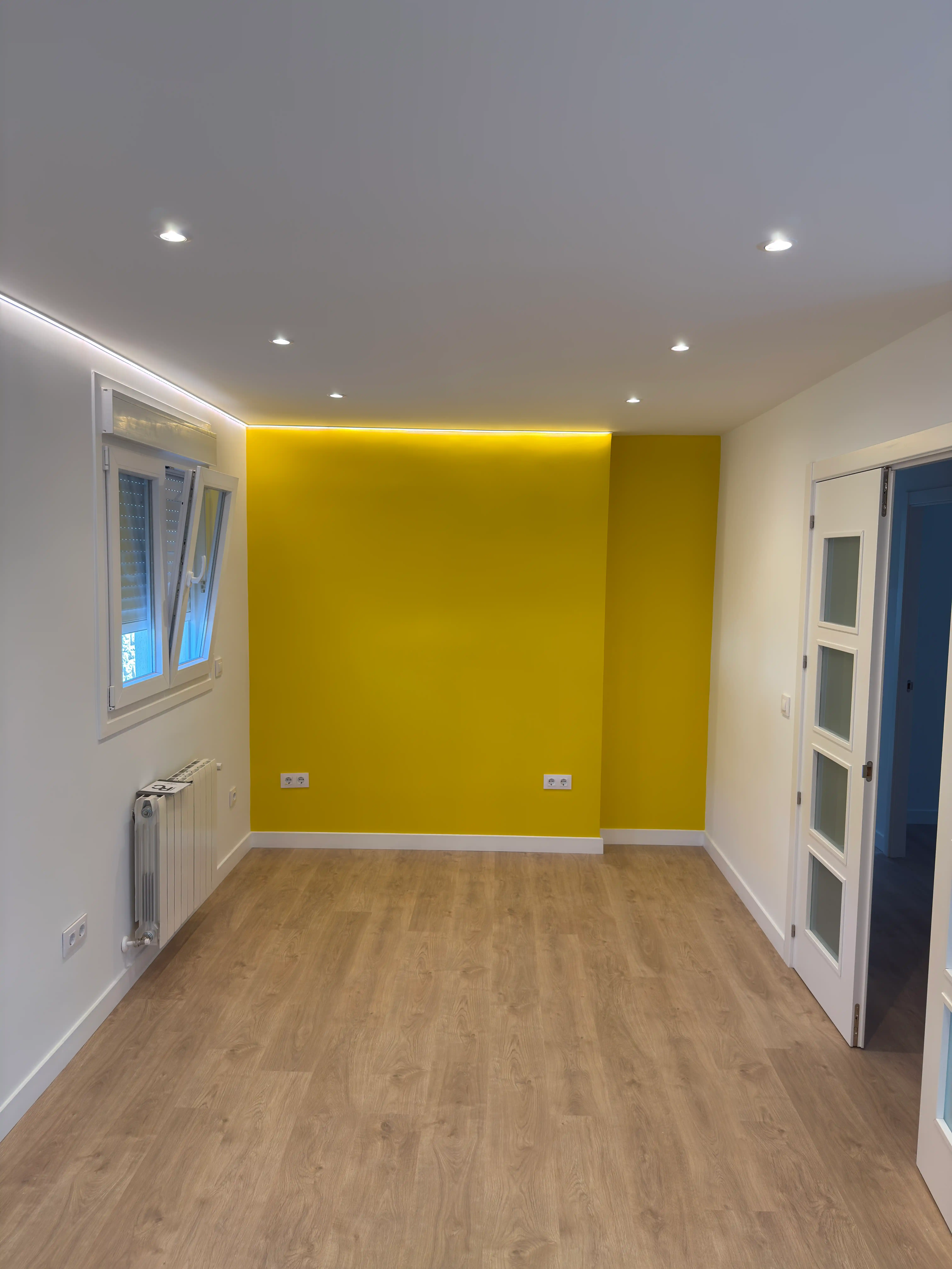 Salón reformado con pared de acento en color amarillo y focos empotrados en el techo.