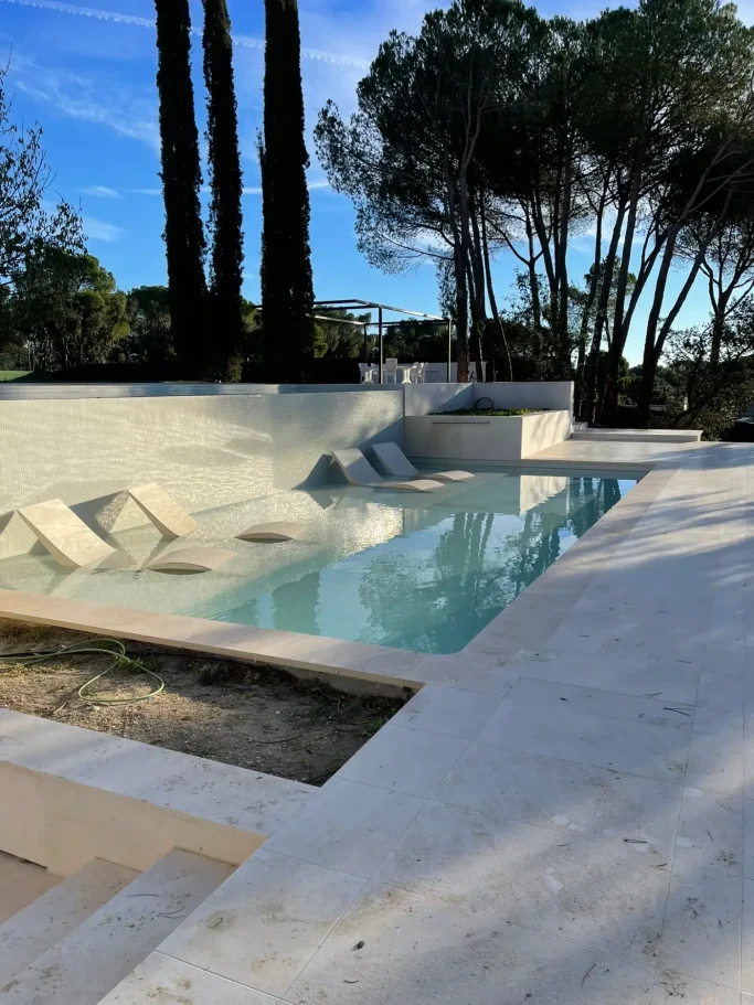 Piscina de Obra con Zona Wellness Construcción de piscina de obra con sillones de hidromasaje integrados en jardín de chalet.